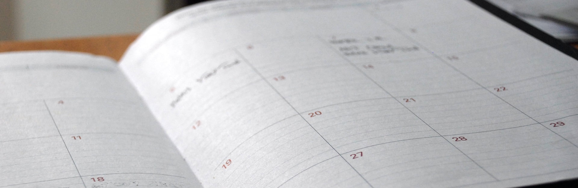 Bildausschnitt, der einen aufgeschlagenen Terminkalender zeigt, der auf einem Schreibtisch liegt